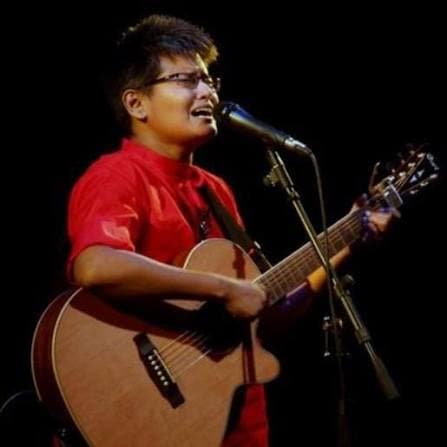 Shayan wearing red and performing with an acoustic guitar