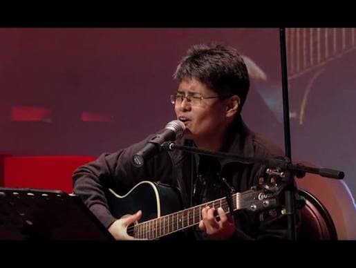 Shayan singing with a guitar under stage lights